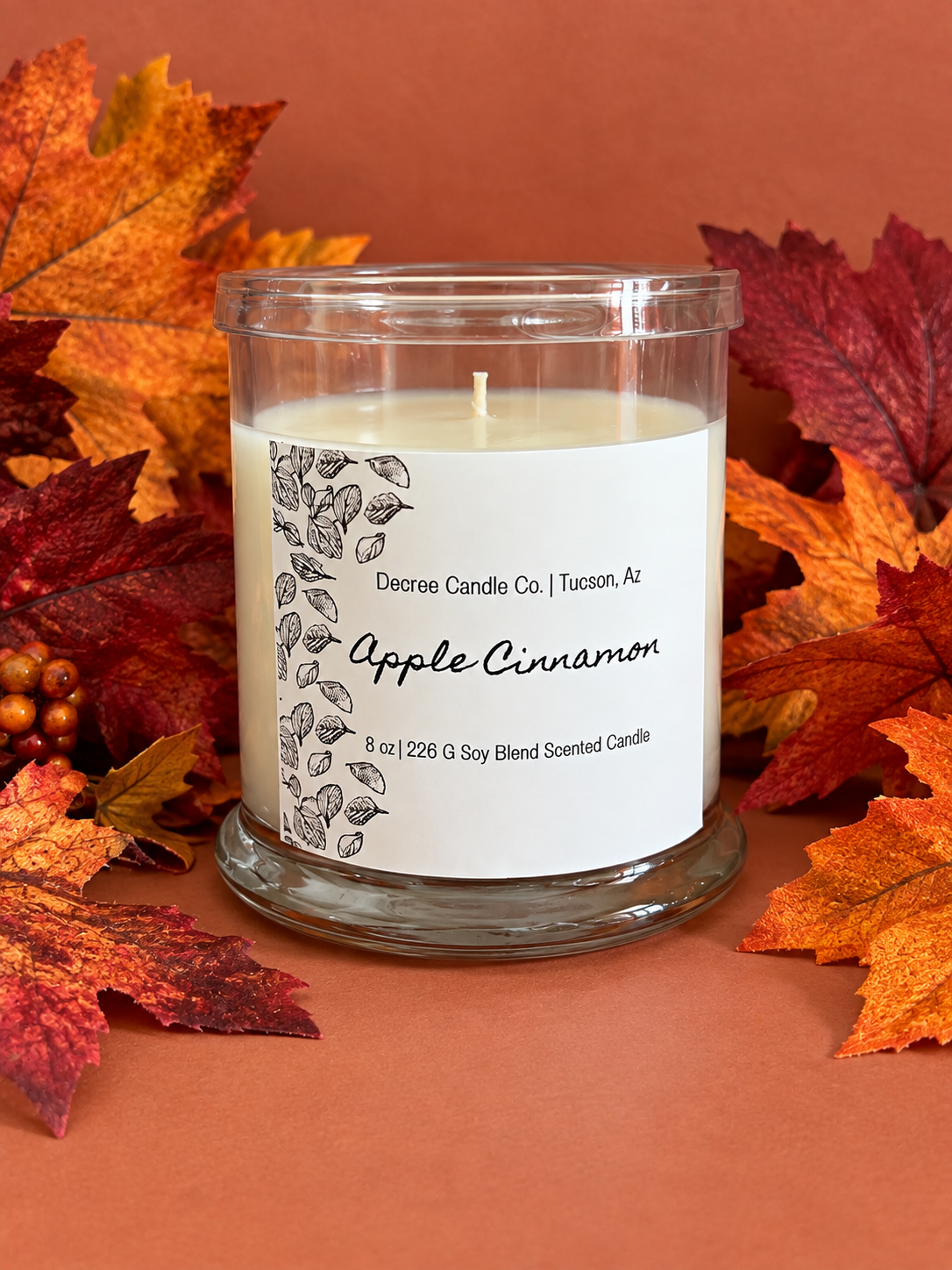 Apple Cinnamon fall scented candle by Decree Candle Co. styled with colorful autumn leaves.