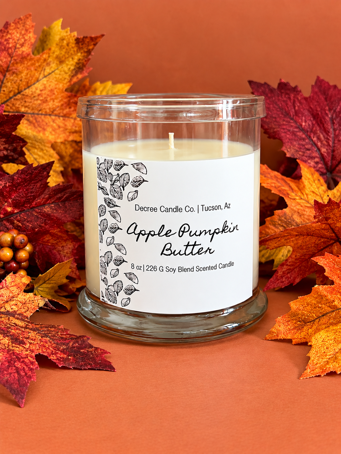 Apple Pumpkin Butter fall scented candle by Decree Candle Co. styled with colorful autumn leaves.